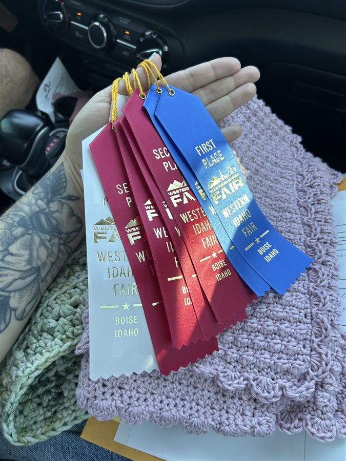 Abby's hand holding four Western Idaho Fair ribbons over a crochet project in progress